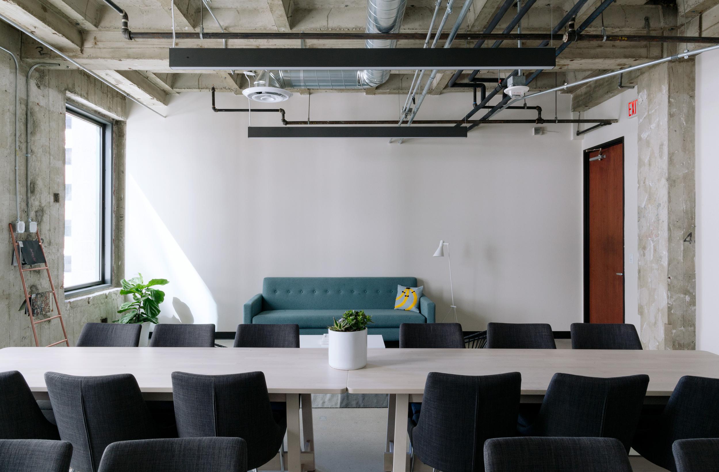 Office interior with a large table and chairs, and a sofa in the background